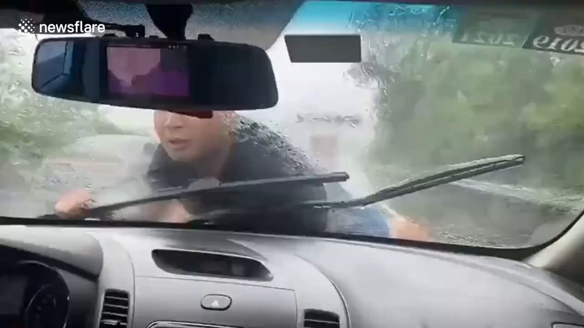 Man washes windshield from outside car during heavy rain